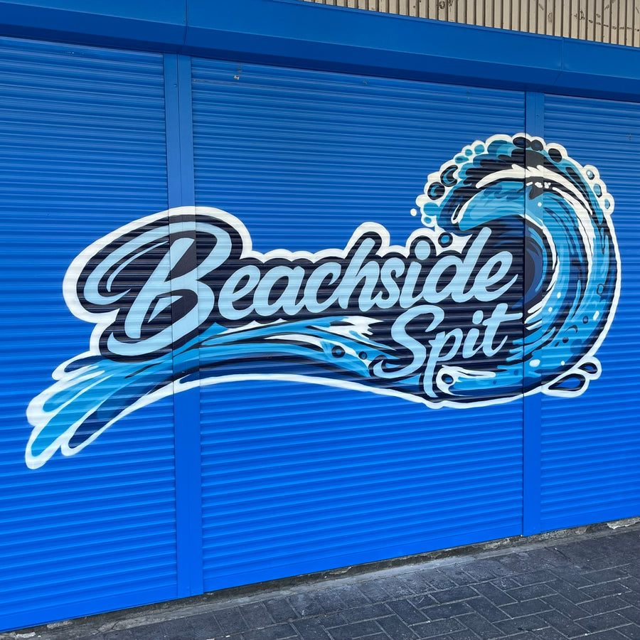 Beachside Spit lettering and ocean wave mural painted across blue roller shutters by DMuly