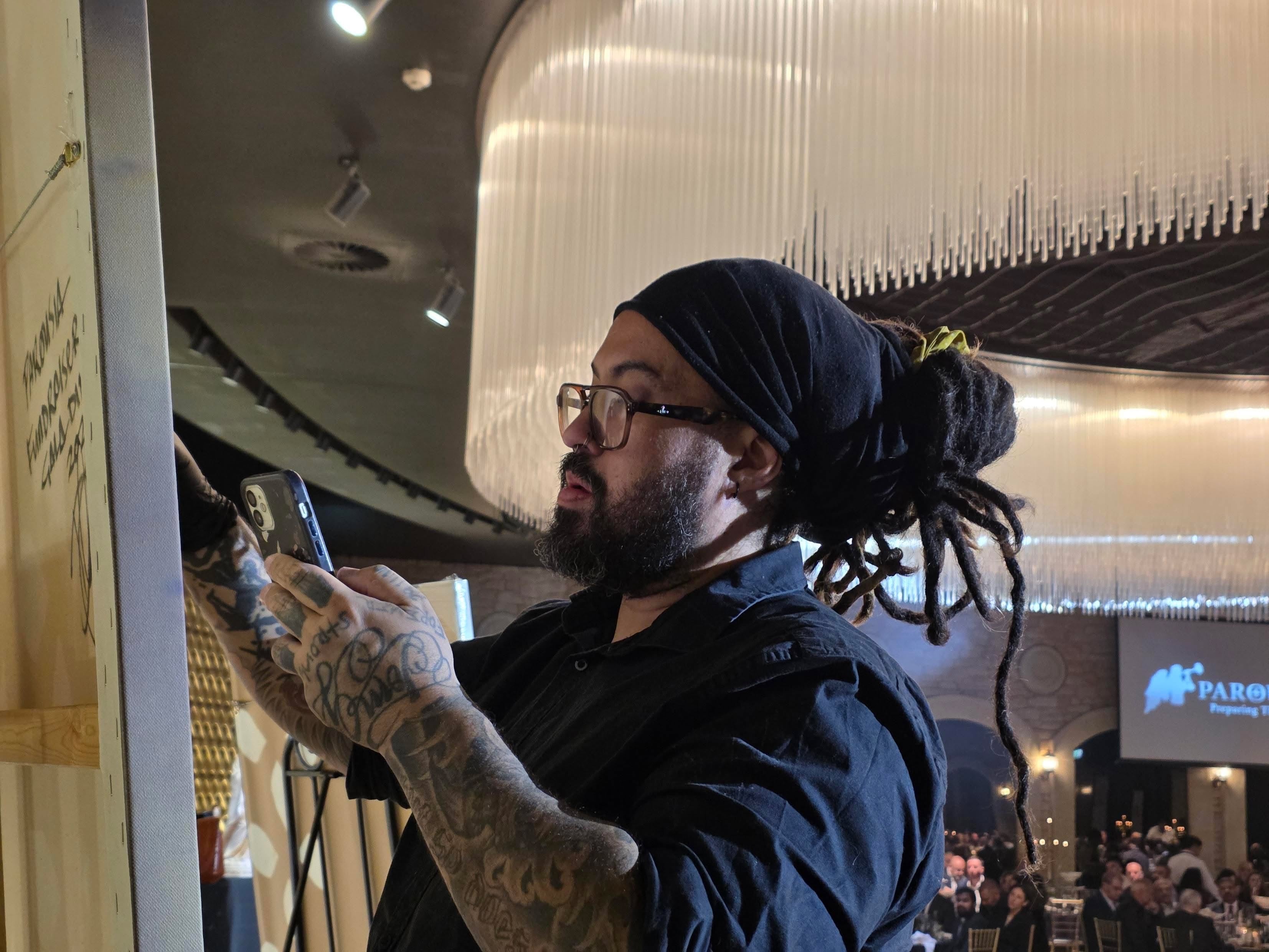 Danny DMuly Mulyono painting at an easel during a live event with guests in the background