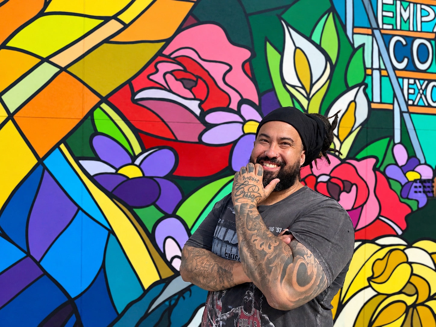 Danny “DMuly” Mulyono smiling in front of his colourful stained-glass-style floral mural.