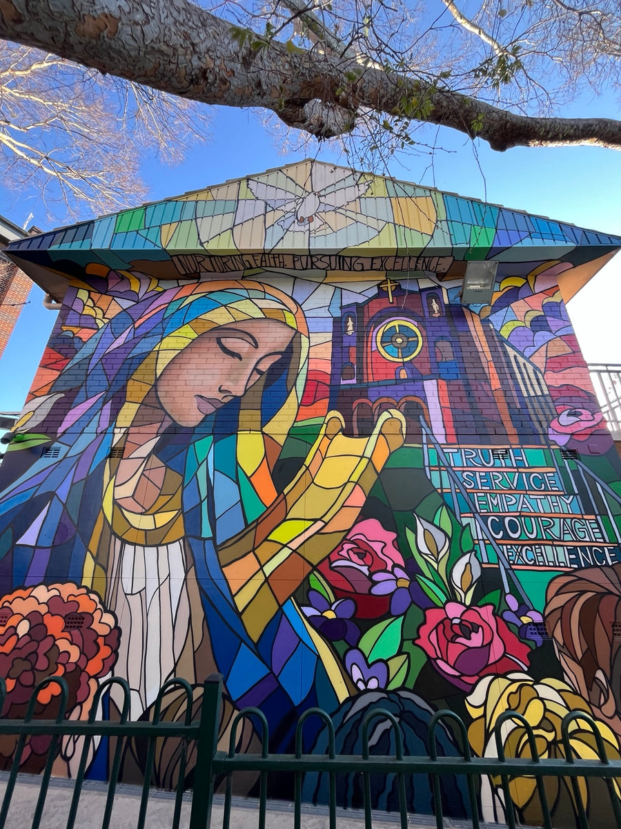 School exterior mural by DMuly with Mary, a dove, flowers and school values in a colourful stained-glass style